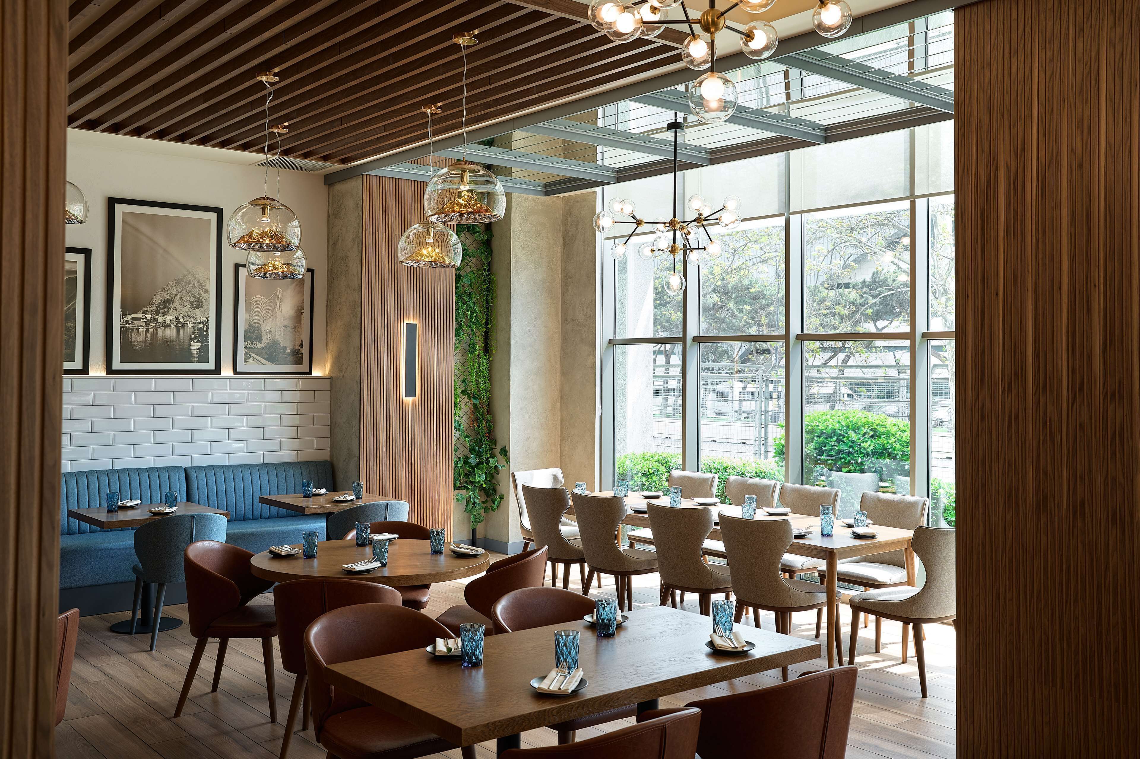 Et moderne restaurantinteriør med træborde og -stole, billeder på væggen og et stort vindue med udsigt over det fri.