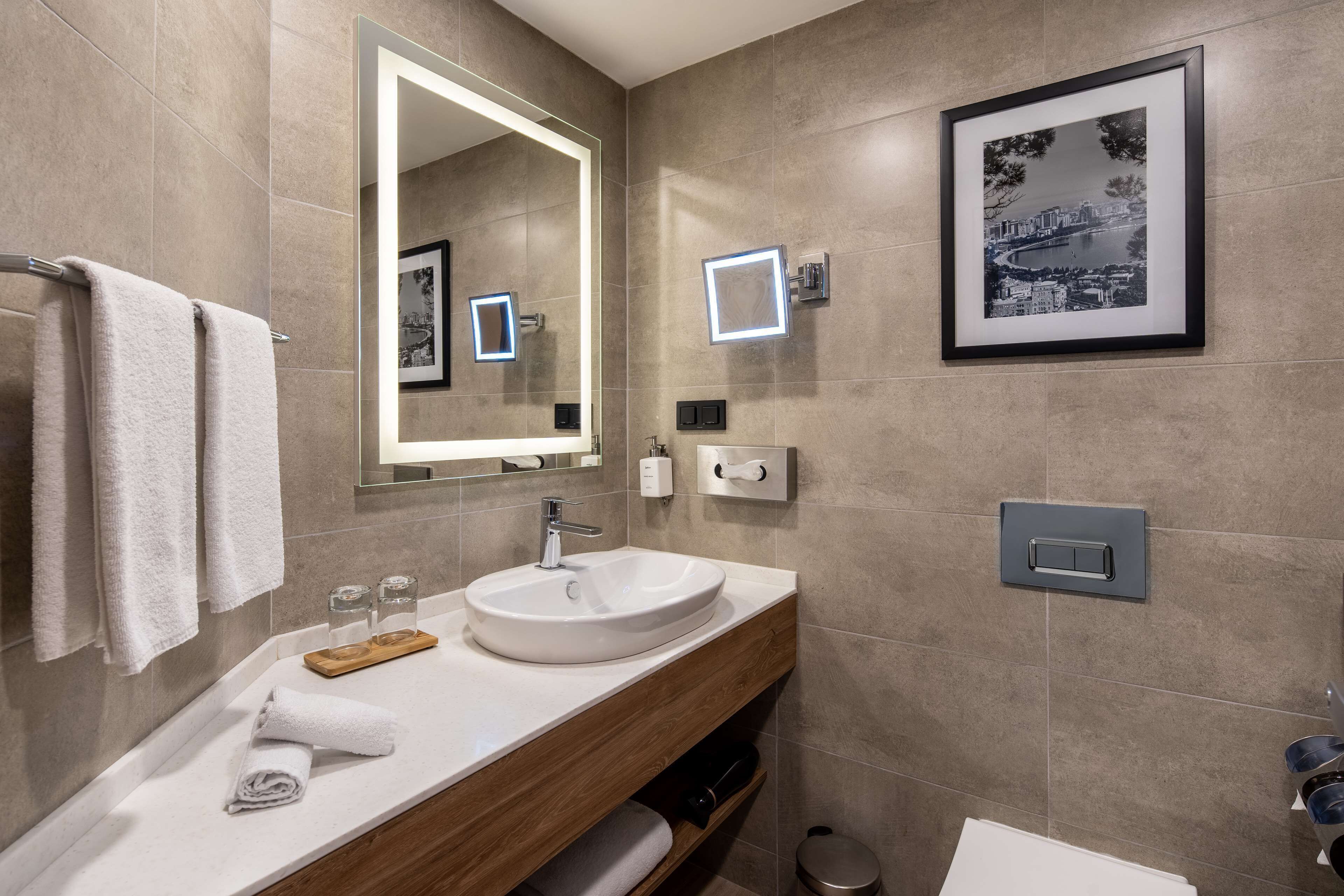 A modern bathroom with a white sink, wooden vanity, and a large mirror.