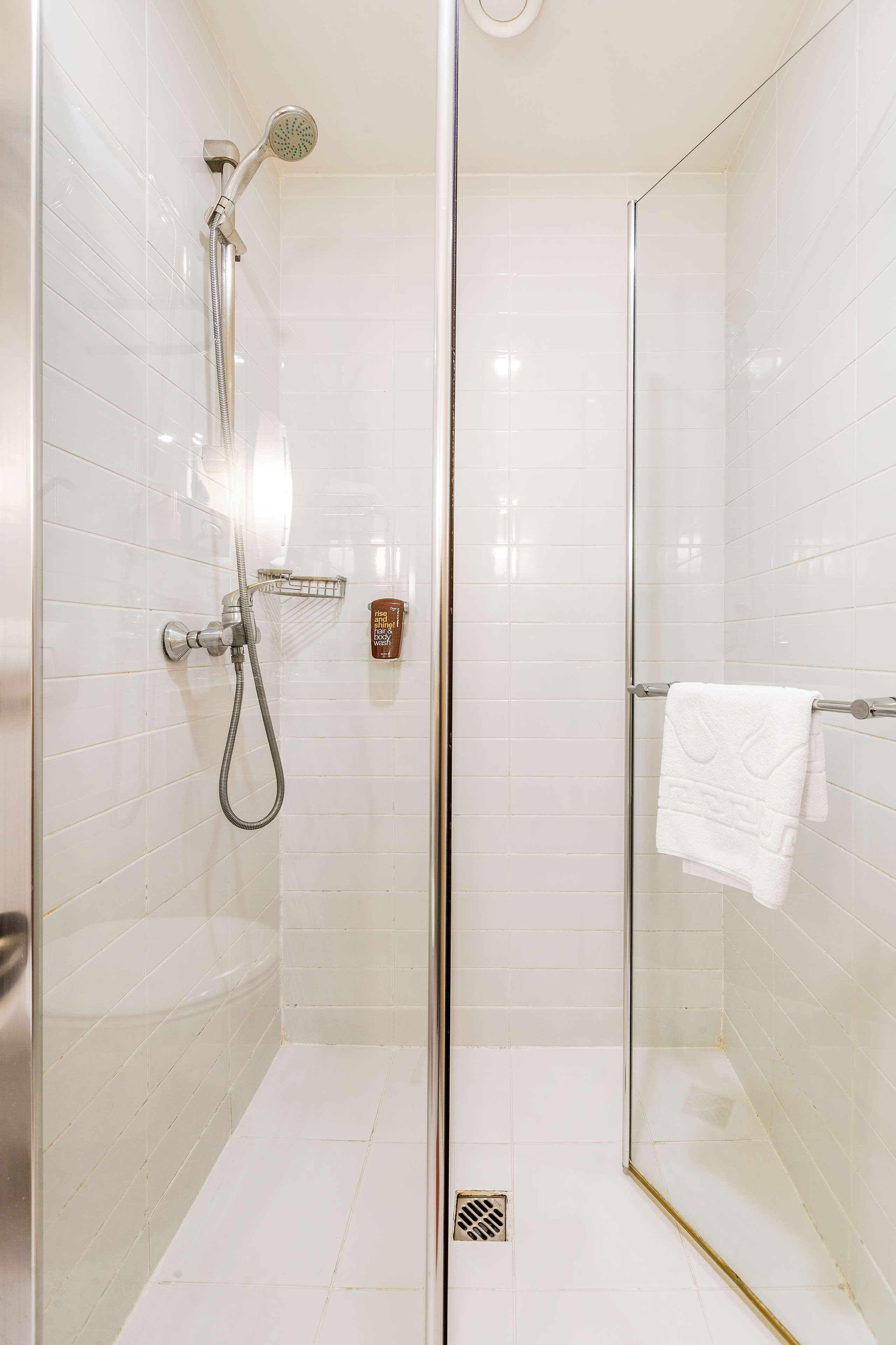Een douchecabine met glazen wanden, een handdouche en een kraan op de muur.