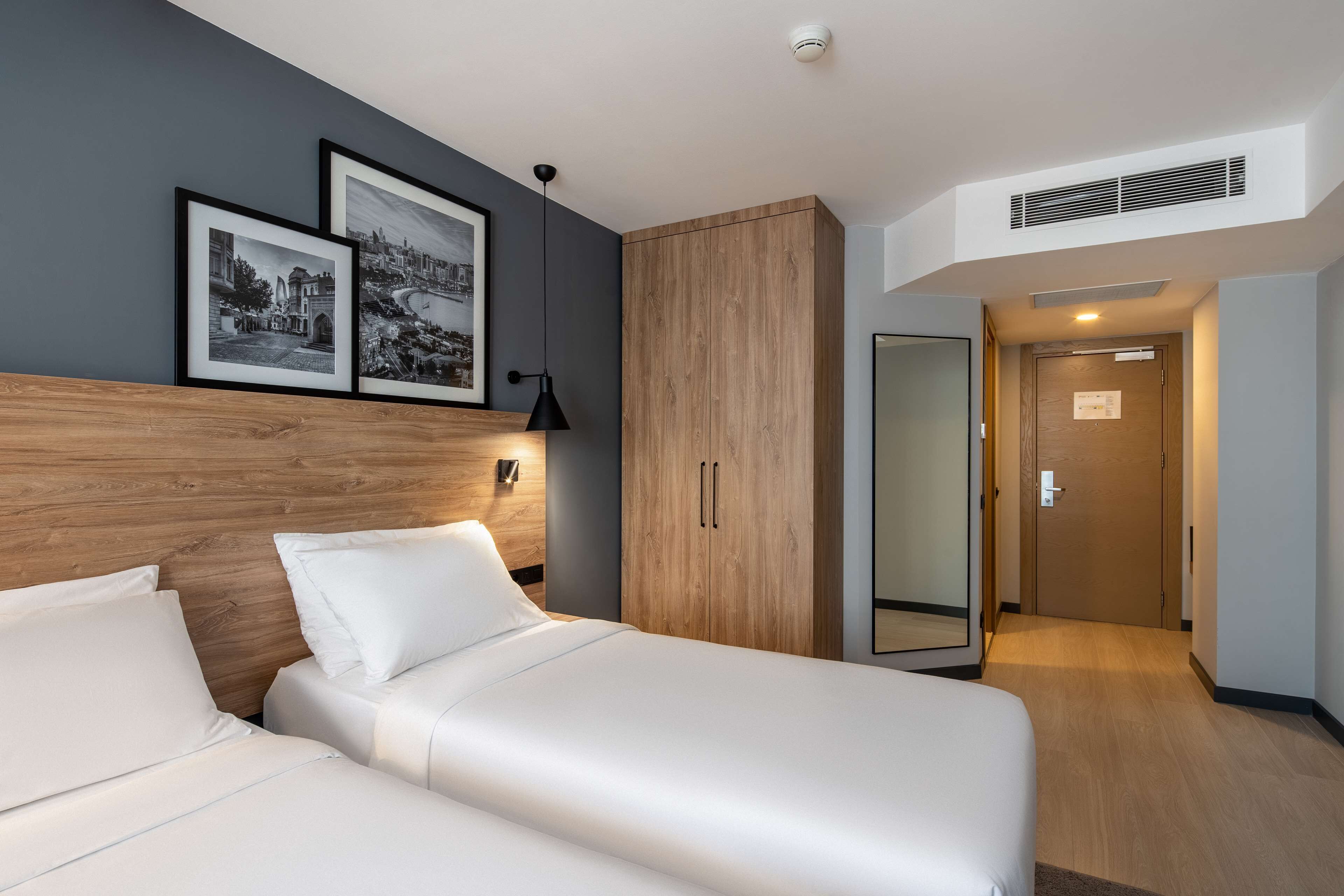 Habitación de hotel con una cama, un armario, un espejo y dos cuadros en la pared.