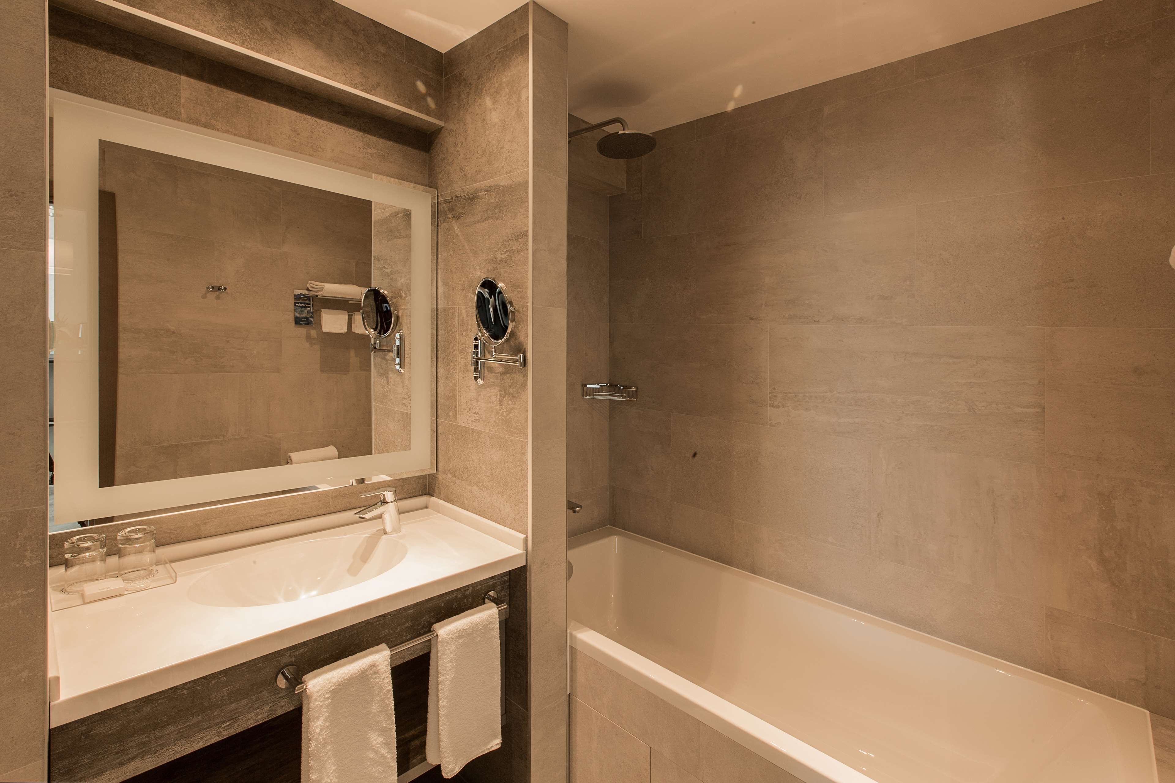 A modern bathroom with a large mirror, a sink, and a walk-in shower.