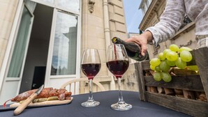A table with two wine glasses, a wooden crate with green grapes, and a charcuterie board with cured meats and pickles.