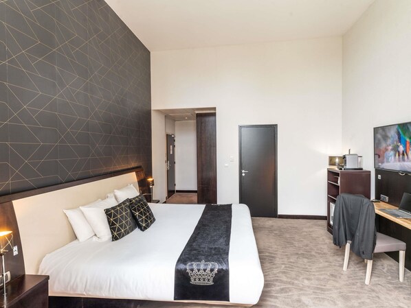 A hotel room with a large bed, a desk, a TV, and a door.