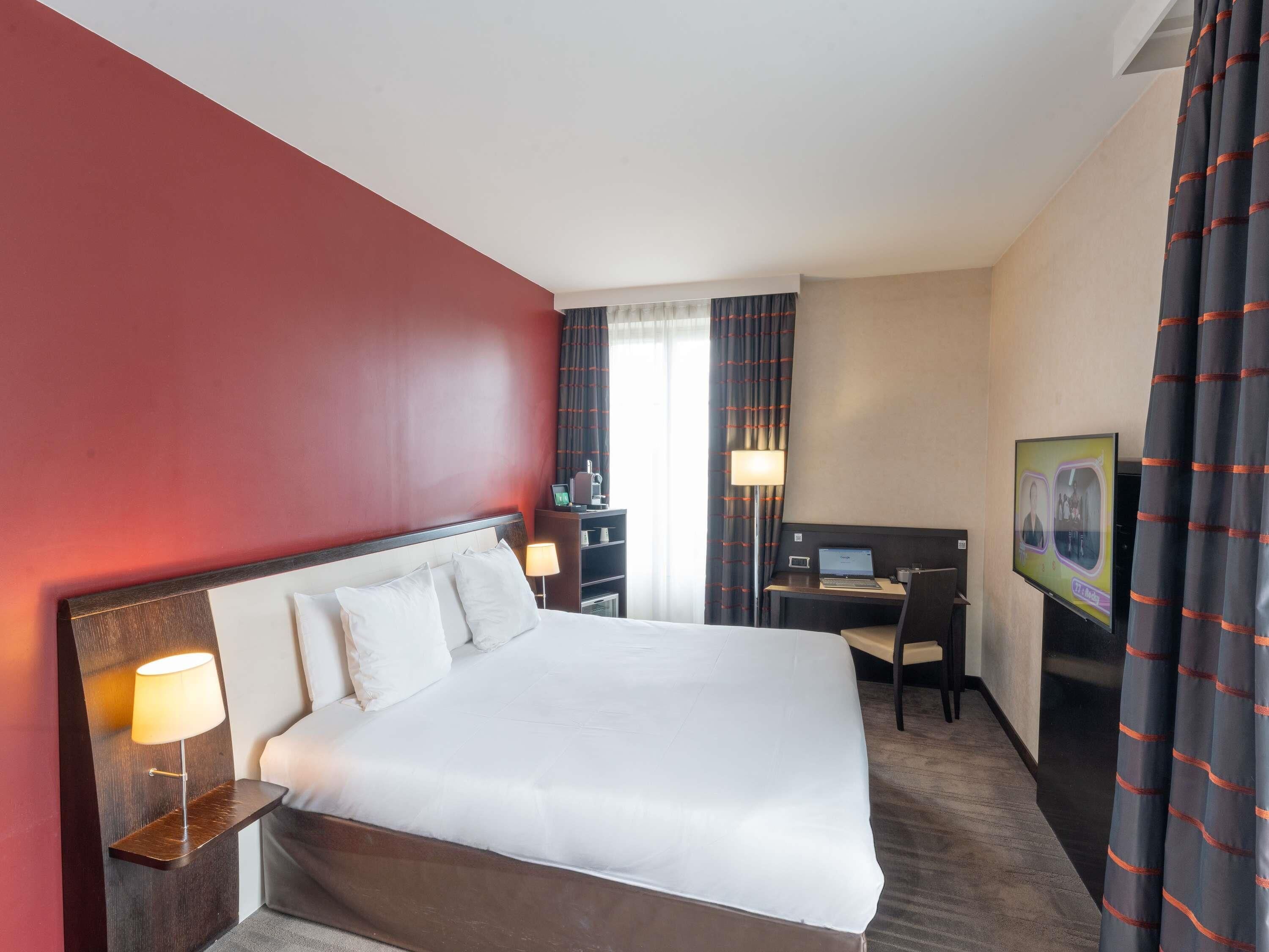 Een hotelkamer met een groot bed, een bureau met een laptop, een stoel en een televisie.