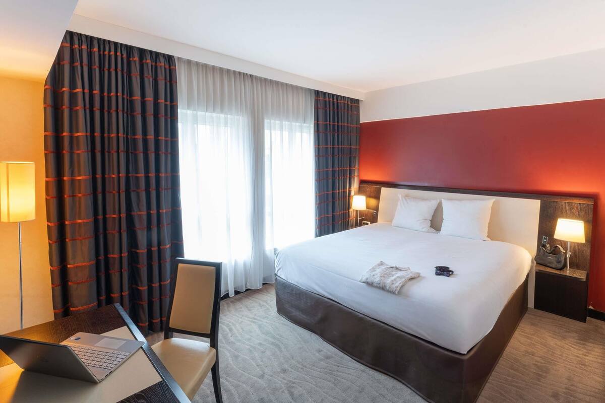 A hotel room with a bed, desk, chair, and two bedside lamps.