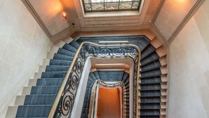 A grand staircase with ornate black and gold railings, a central open landing, and a stained glass window above.