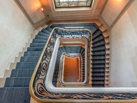 A grand staircase with ornate black and gold railings, a central open landing, and a stained glass window above.