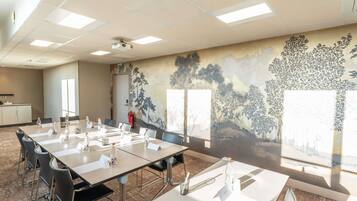 Una sala de conferencias con una larga mesa, sillas, un proyector y un mural en la pared.