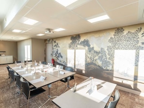 A conference room with a long table, chairs, a projector, and a mural on the wall.