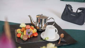 A tray with food, a teapot, and a cup on a table with a bed and a handbag in the background.