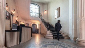A grand lobby with a marble floor, a staircase, and a reception desk.