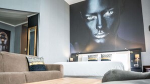 A modern hotel room with a large bed, a sofa, a wooden coffee table, and a large wall mural.