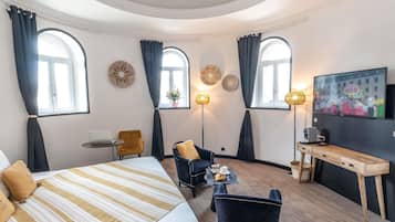 Une chambre d’hôtel avec un lit, un bureau, une chaise, une télévision et deux fenêtres avec des rideaux.