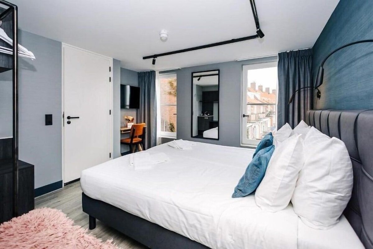 A modern bedroom with a large bed, a desk, and a view of the city.