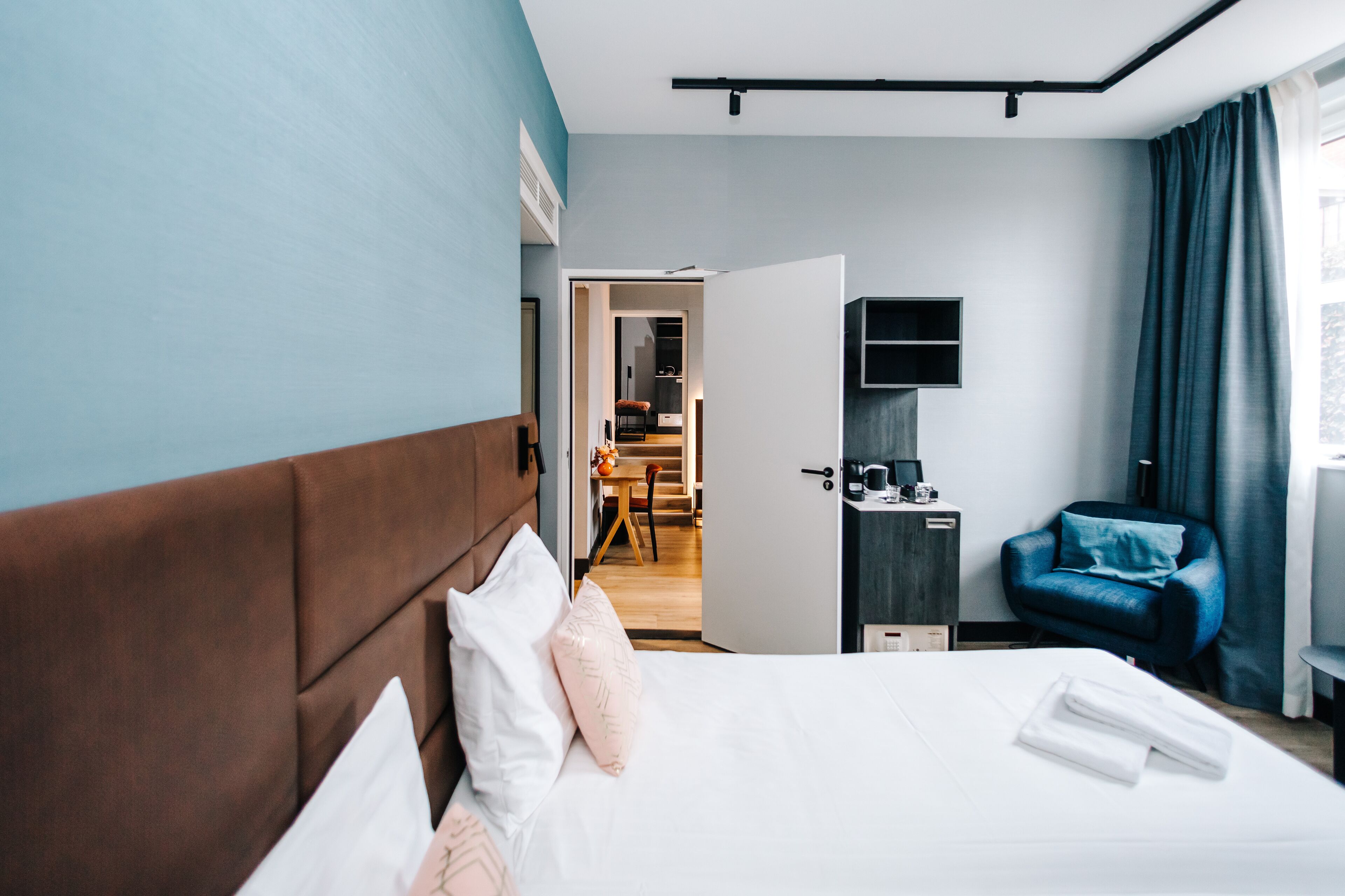 A hotel room with a bed, a desk, a chair, and a view of the dining area.