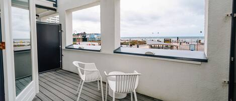 A balcony with a view of the beach, a table, and two chairs.