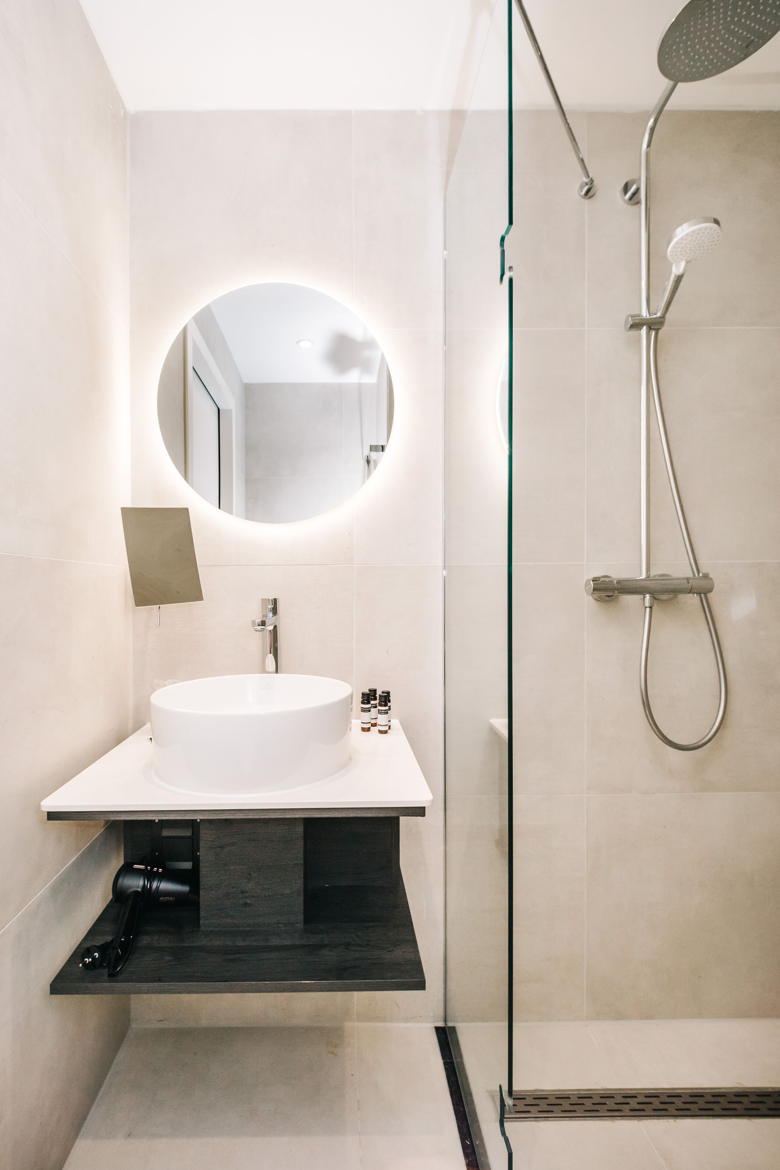 Un bagno moderno con uno specchio rotondo, un lavandino bianco e una doccia con pareti in vetro.