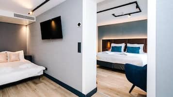 A modern hotel room with a bed, a seating area, a flat-screen TV, and a ceiling-mounted light fixture.