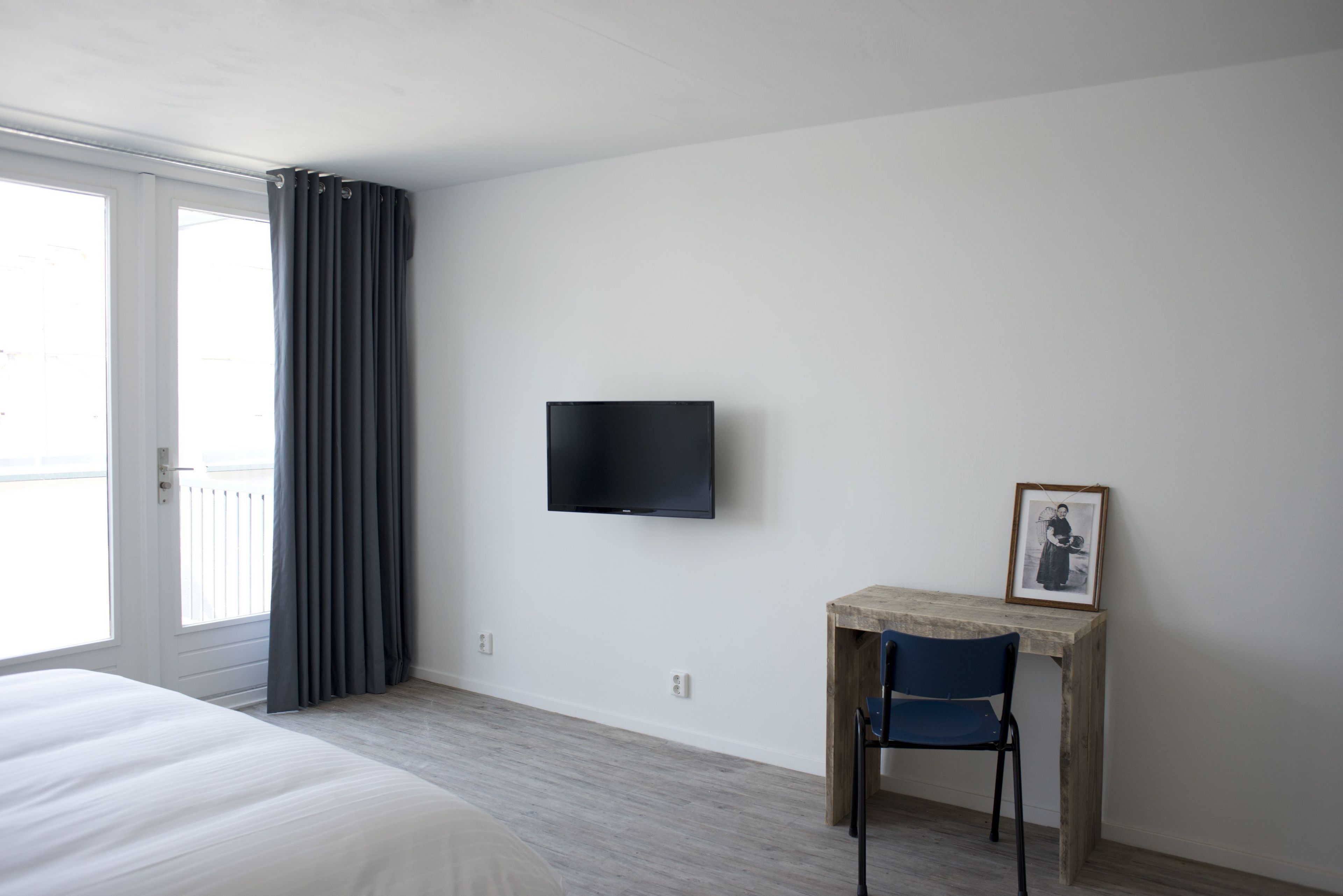 A hotel room with a bed, a desk with a chair, a television, and a window with curtains.
