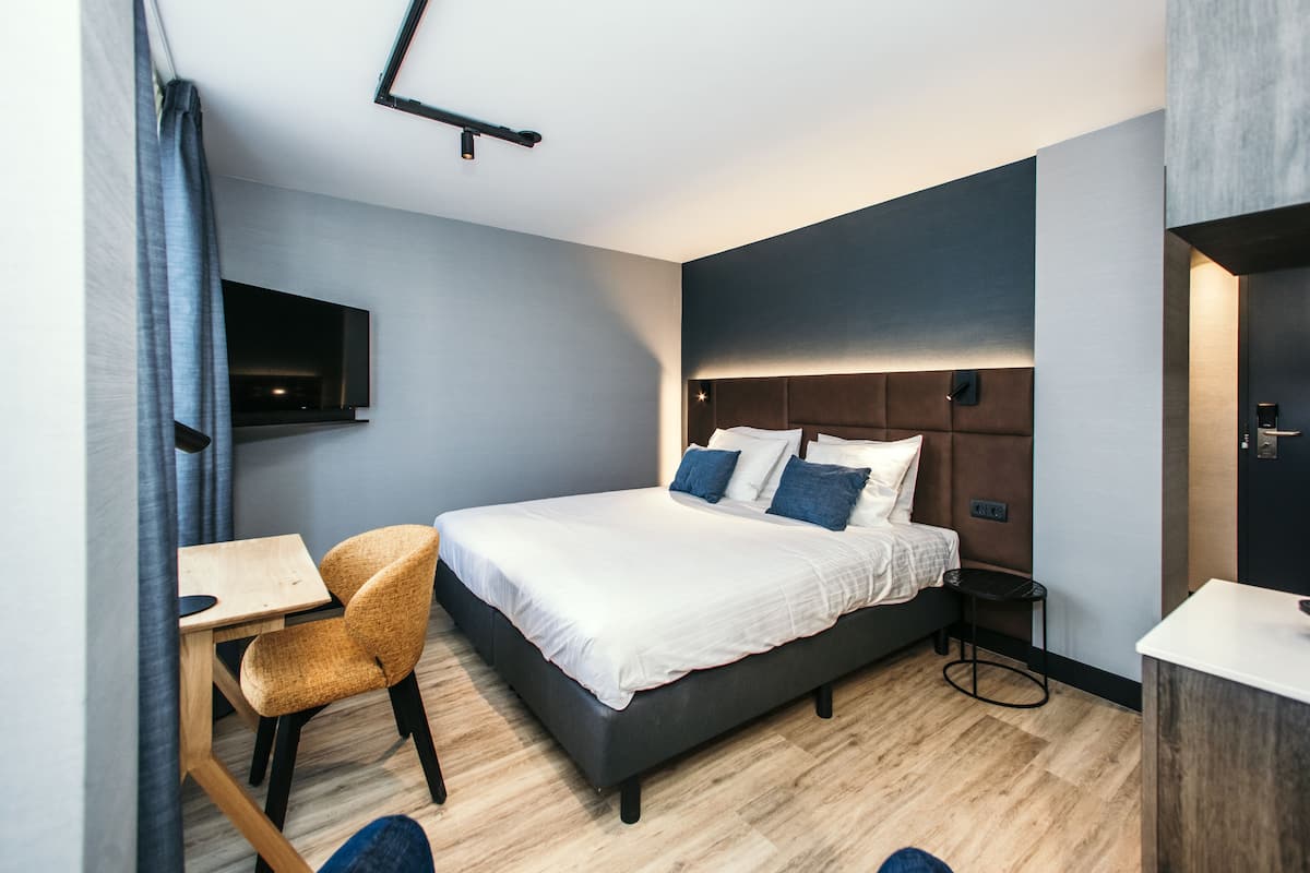Une chambre d’hôtel moderne, dotée d’un grand lit, d’un bureau, d’une chaise et d’un téléviseur fixé au mur.
