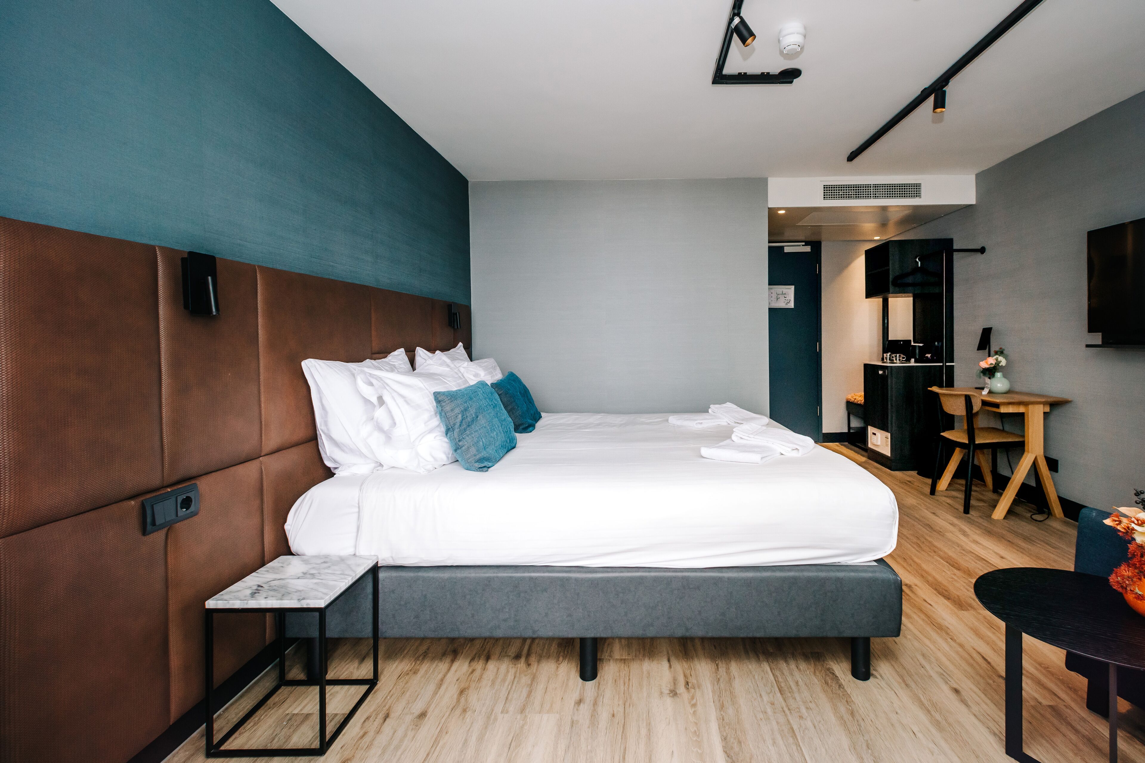Une chambre d’hôtel moderne dotée d’un grand lit, d’une table de chevet, d’un petit bureau et d’un téléviseur à écran plat fixé au mur.