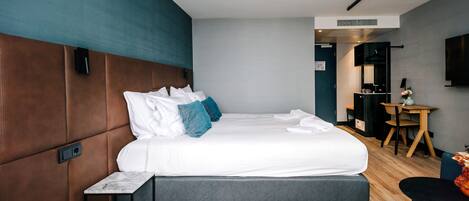 Une chambre d’hôtel moderne dotée d’un grand lit, d’une table de chevet, d’un petit bureau et d’un téléviseur à écran plat fixé au mur.