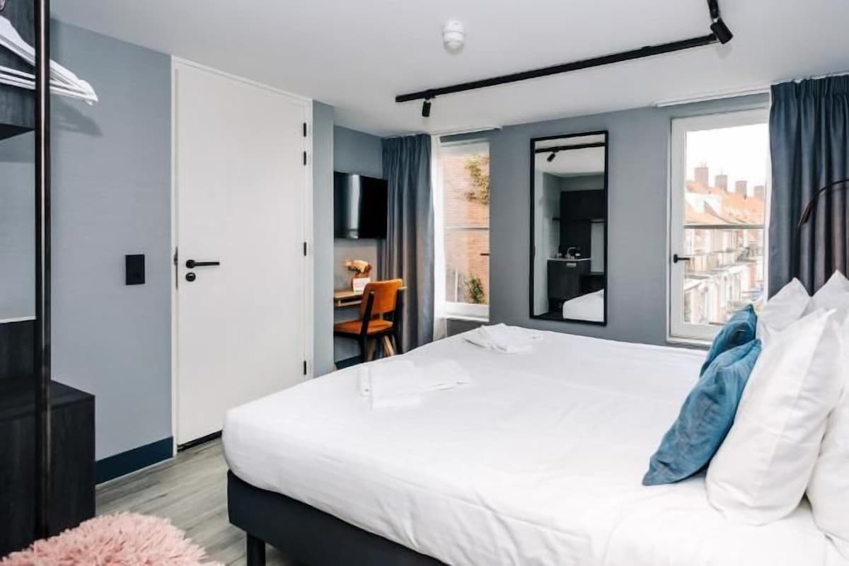 A modern hotel room with a large bed, a desk, and a view of the city.