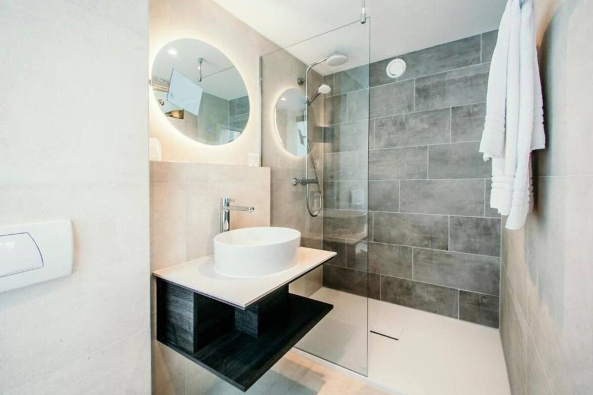 Une salle de bain moderne avec un grand miroir rond, un lavabo blanc et une douche à parois de verre.