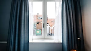 A window with dark curtains, a view of buildings outside, and a door with a handle. - Amsterdam Beach Hotel (Zandvoort)