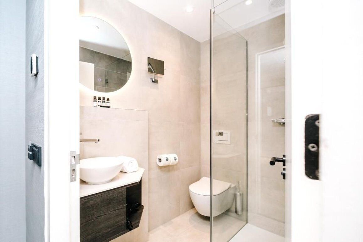A modern bathroom with a glass shower enclosure, a round mirror, a white sink, and a toilet.