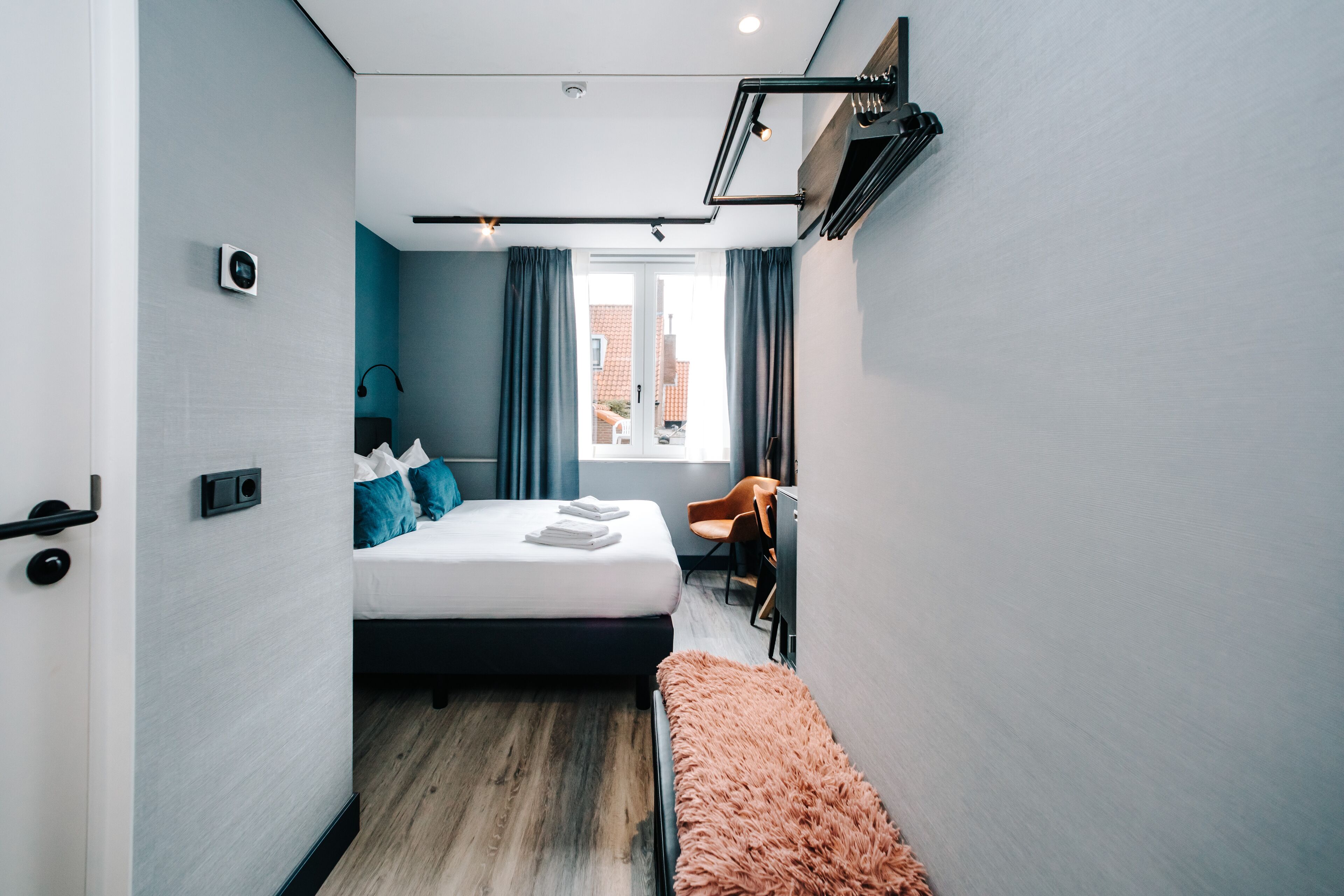 A modern hotel room with a bed, a desk, and a bench.