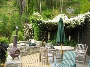 Um deck de madeira com lareira de pedra, área de estar ao ar livre e um guarda-sol verde.