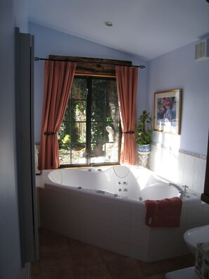 Um banheiro com uma banheira grande, uma janela com cortinas, uma planta em vaso e um quadro na parede.