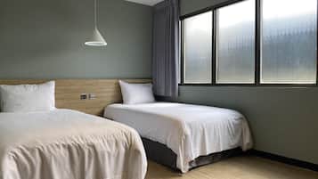 Een hotelkamer met twee bedden, een houten hoofdeinde, een groot raam met gordijnen en een hanglamp.