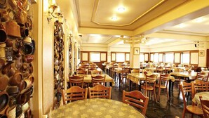 A large dining hall with multiple tables and chairs, a wall with numerous ceramic pots, and a ceiling with recessed lighting. - Prince Hotel (Jiaoxi)