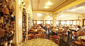 A large dining hall with multiple tables and chairs, a wall with numerous ceramic pots, and a ceiling with recessed lighting. - Prince Hotel (Jiaoxi)
