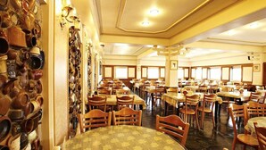 Une grande salle à manger avec de nombreuses tables et chaises, un mur orné de nombreux pots en céramique et un plafond doté d’un éclairage encastré.