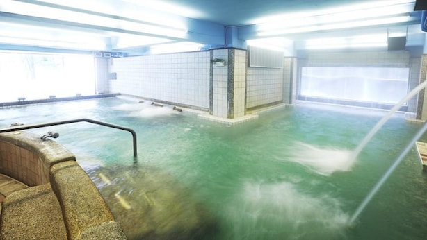 Une grande piscine intérieure avec un banc en bois et une rambarde en métal.