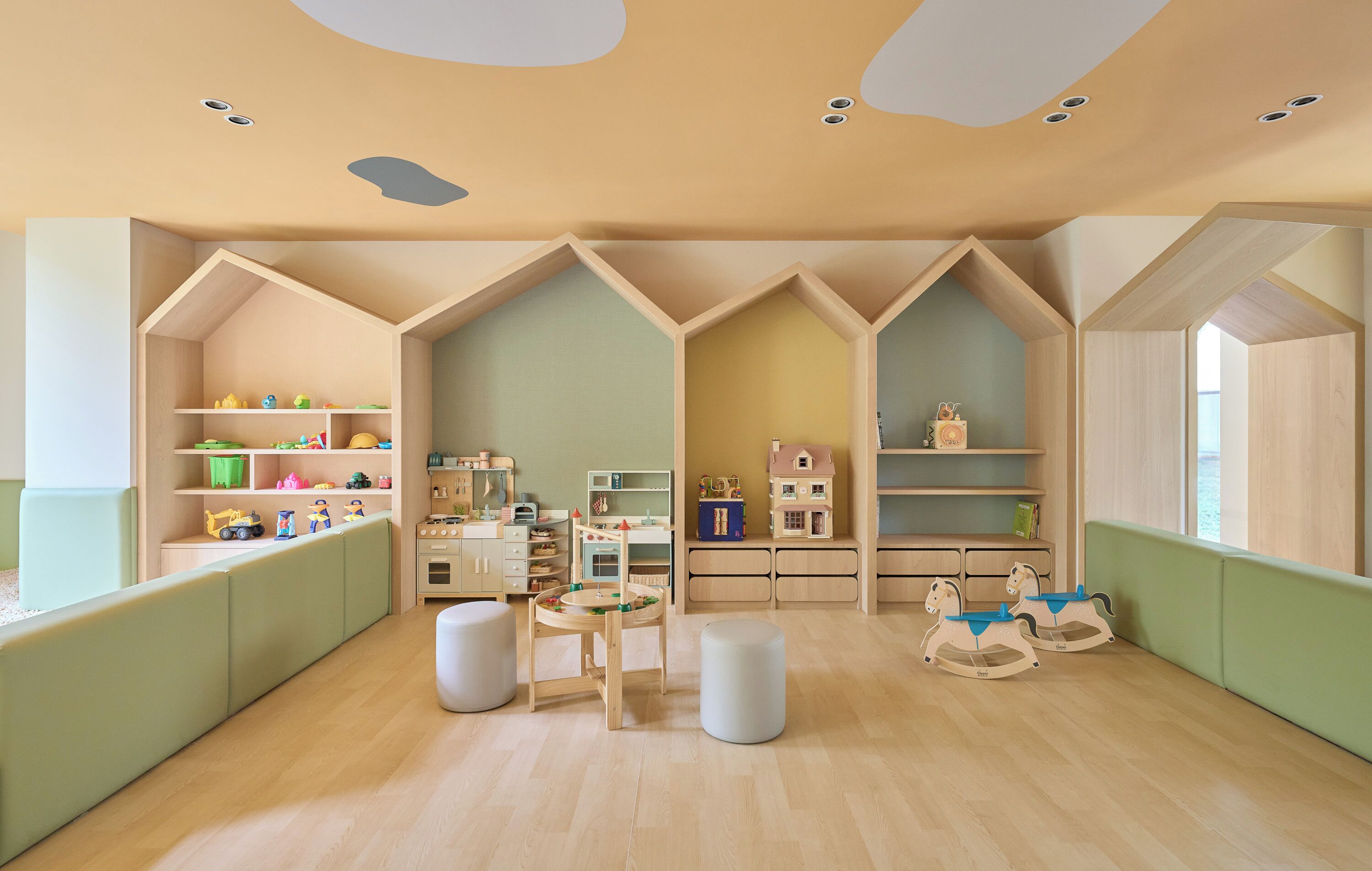 A children's playroom with wooden shelves, a play table, and rocking horses.