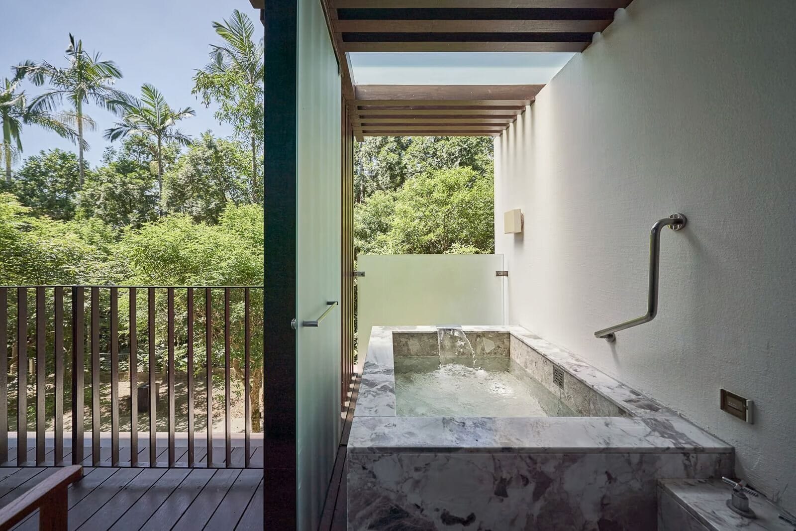 Een wellnessruimte met een jacuzzi, houten terras en uitzicht op weelderige begroeiing.