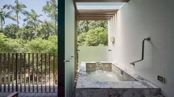 Een wellnessruimte met een jacuzzi, houten terras en uitzicht op weelderige begroeiing.