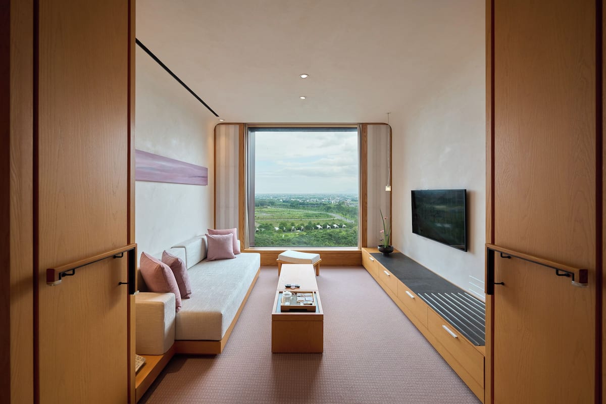Una habitación moderna con un ventanal grande, un sofá, una mesa de centro y un televisor de pantalla plana.