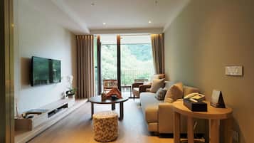 A modern living room with a sofa, a coffee table, a TV mounted on the wall, and a balcony with curtains.