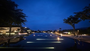 Une vue nocturne d’une piscine, entourée d’arbres, avec un bâtiment doté d’une terrasse.