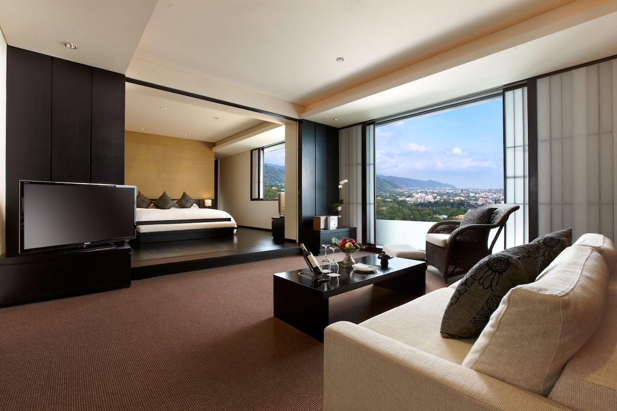 Una habitación de hotel moderna con una cama grande, televisión, sofá y balcón con vista a la ciudad.