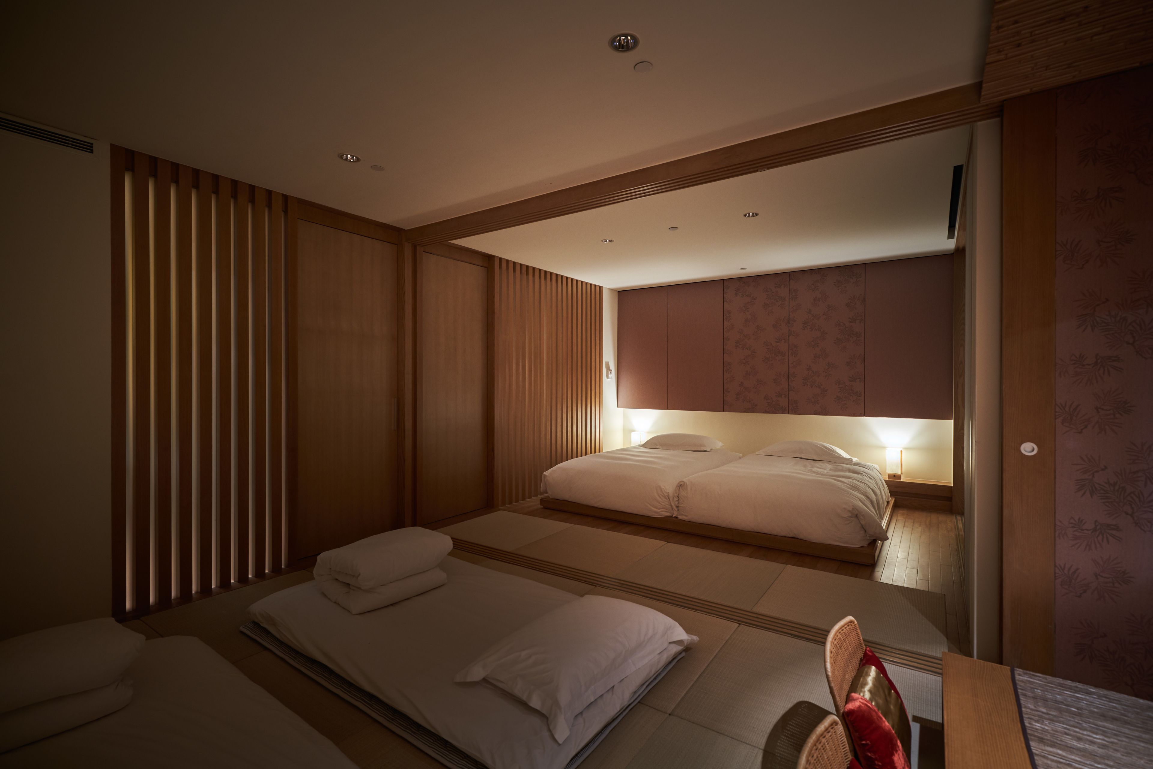 A modern hotel room with two beds, a sitting area, and a large mirror.