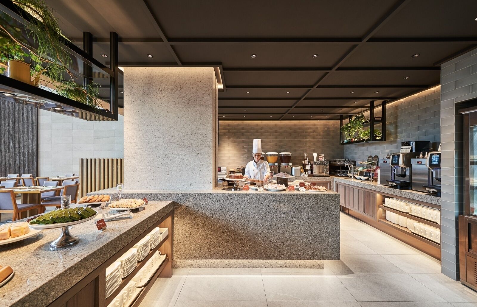 Un restaurante moderno con un chef preparando comida, una barra de buffet con diversos platos y una cafetería con varias máquinas de caf é.