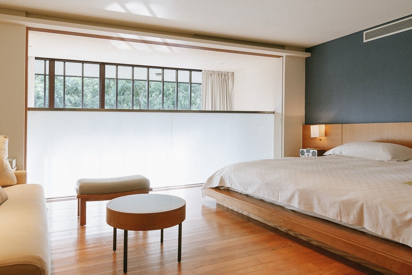 A bedroom with a large bed, a small round table, a chair, and a window with curtains.