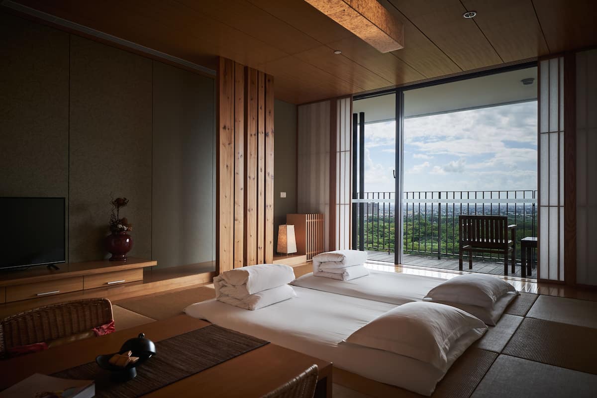 Habitación de hotel con dos camas, televisión, ventana grande y balcón con vistas.