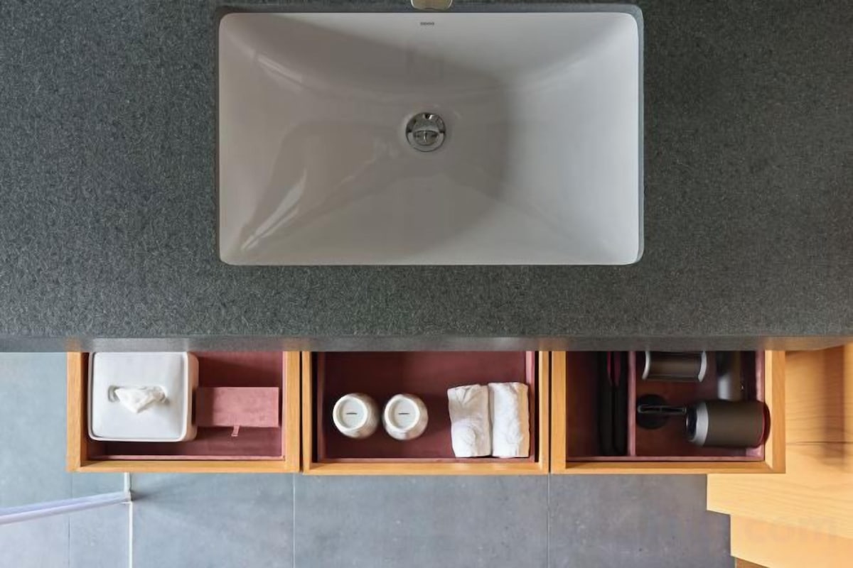 Un baño con lavamanos blanco, espejo y un mueble de madera inferior con artículos de aseo.